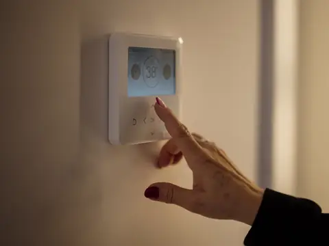 A hand adjusting a wall thermostat