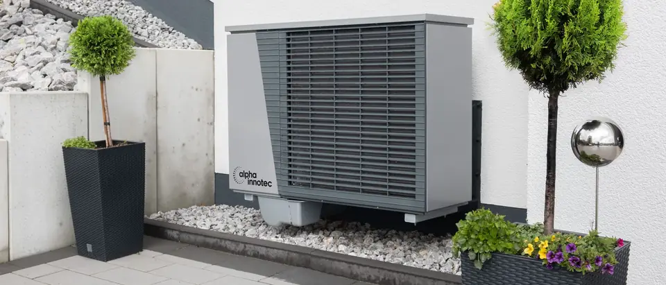 A new outdoor heat pump unit set on gravel beside a white wall with potted plants
