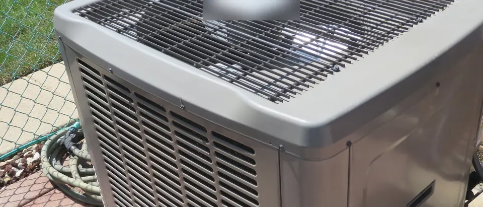 A central air conditioning condenser on a concrete pad in sun