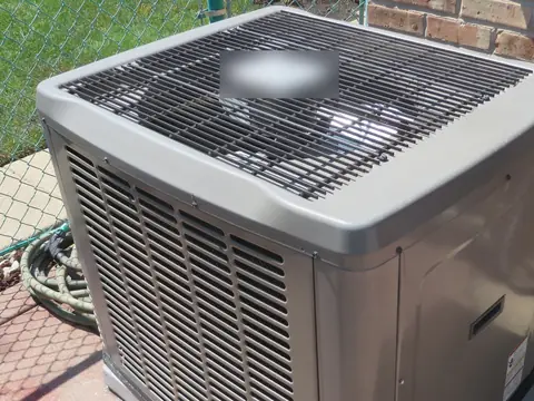 A central air conditioning condenser on a concrete pad in sun