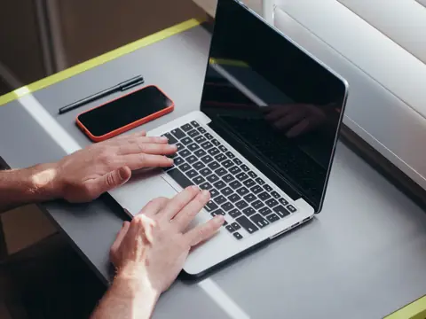 Typing on a laptop at a sunny desk