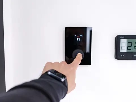 A finger setting a wall thermostat