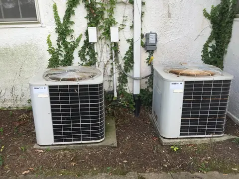 Two outdoor AC units against a light house wall