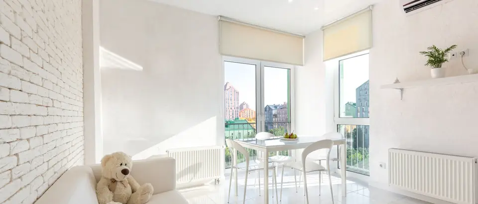 A sunlit white living room with an air conditioner high on the wall
