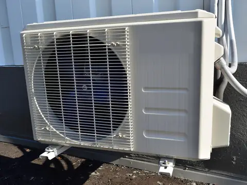 A compact outdoor AC unit in the sun beside a house