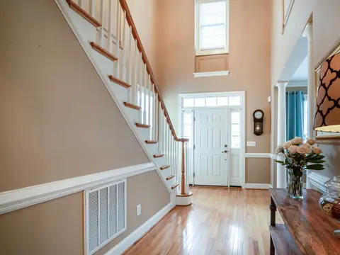 A return air grille low on the wall of a sunny entry hall