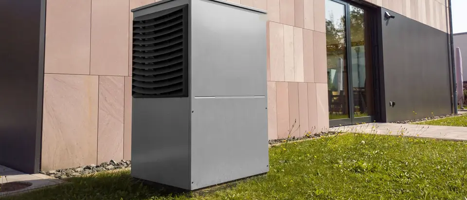 A modern heat pump outdoor unit on a lawn beside a house