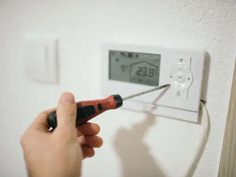 A wall thermostat being set with a screwdriver