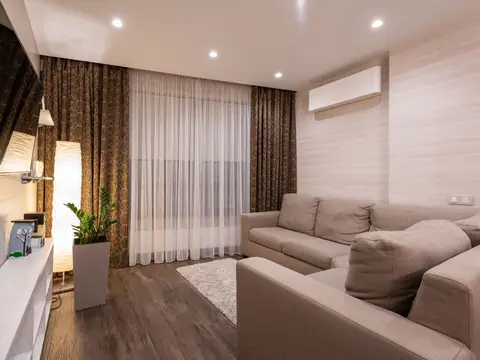 A living room with sheer curtains drawn and a ductless AC on the wall