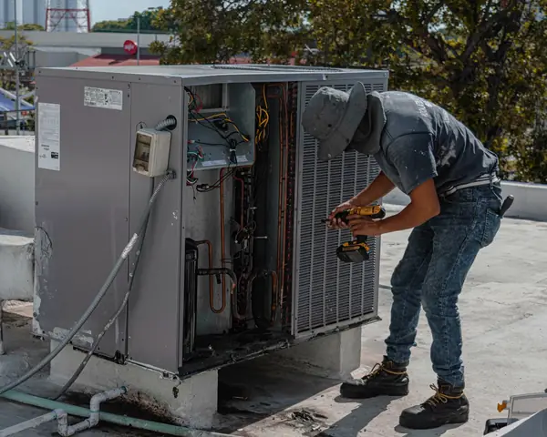 A technician working on an outdoor air conditioning condenser in bright sun