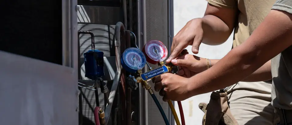 Hands connecting refrigerant gauges to an outdoor AC unit