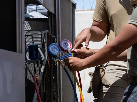 Hands connecting refrigerant gauges to an outdoor AC unit