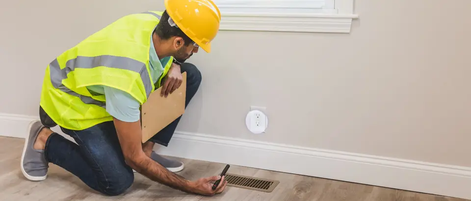 A worker checking a floor air vent in a bright room