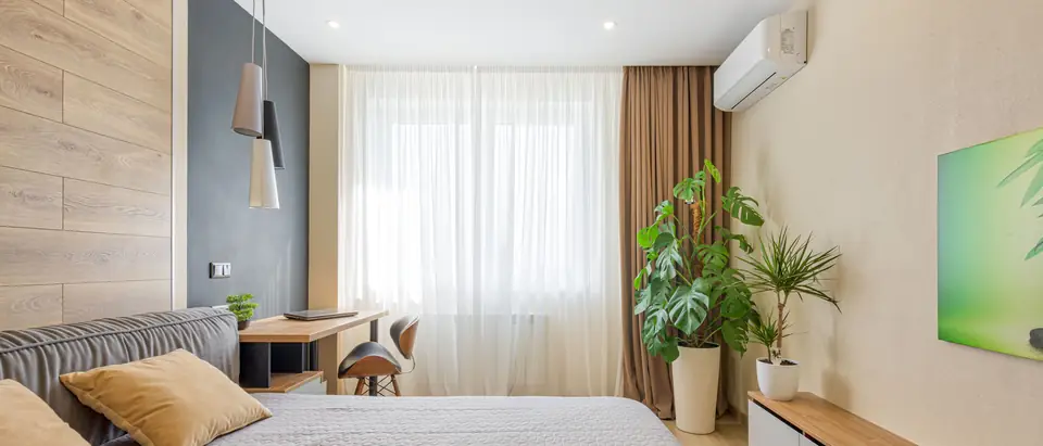 A bright bedroom with a ductless air conditioner above the curtains