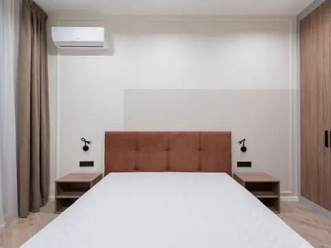 A ductless AC head high on the wall above a bed