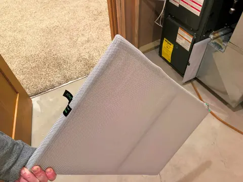A hand holding an air filter pulled from beside the furnace