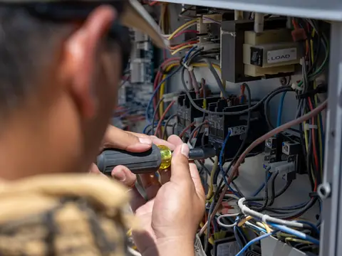 Hands with a screwdriver at the wiring panel of an AC unit